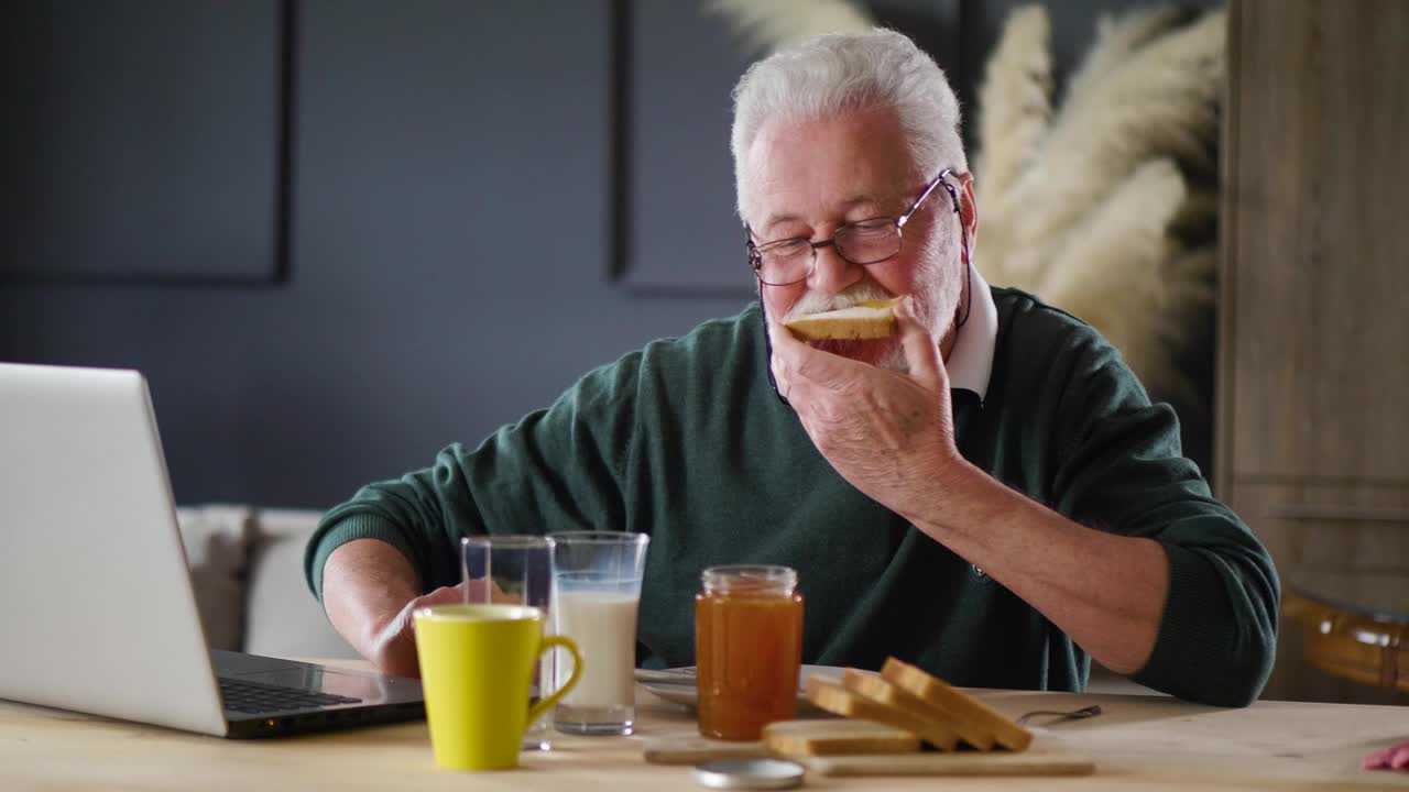 一位70多岁的退休老人边吃早餐边用笔记本电脑看新闻视频下载