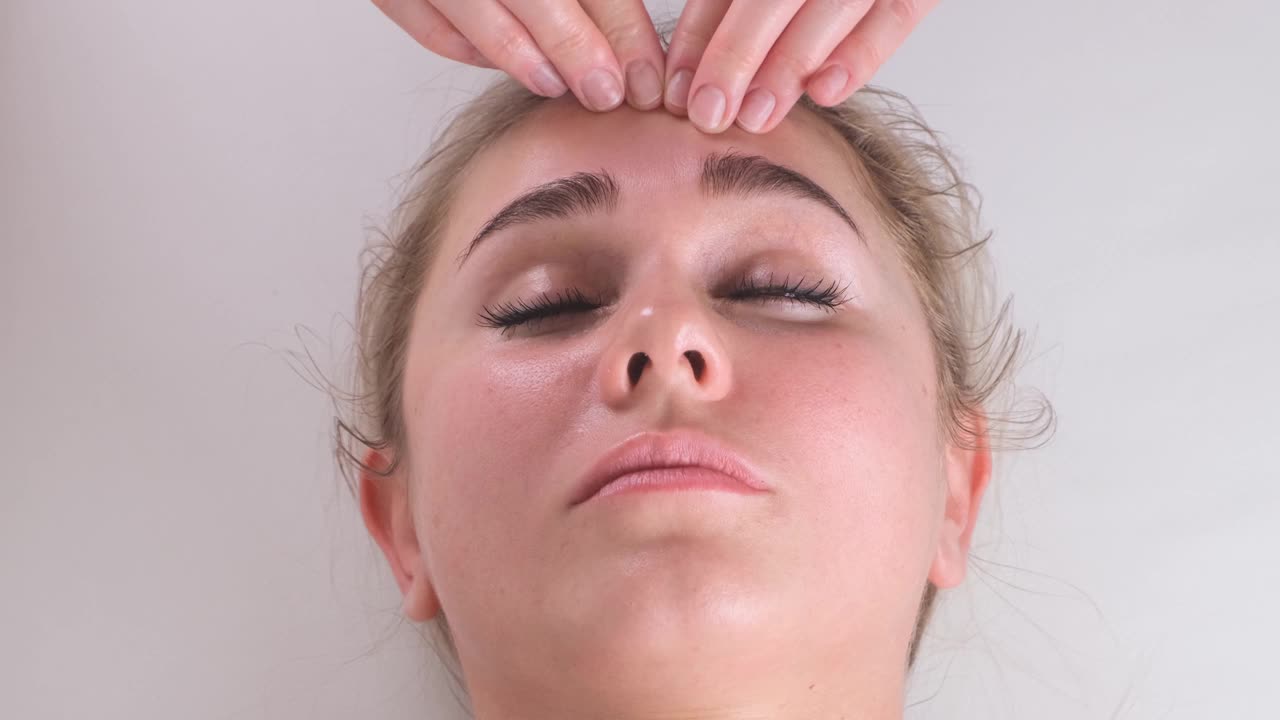 面部按摩美容治疗。一个年轻女人的脸躺在背上，得到面部提升按摩，捏和卷技术视频下载