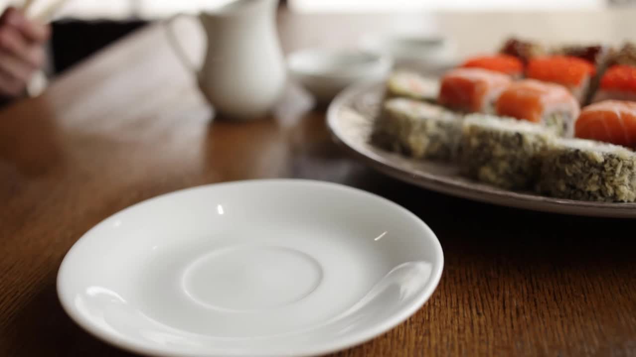 日本寿司卷在咖啡馆餐厅。酱油，木棒，芥末，姜。一张桌子，一扇俯瞰城市的窗户。晚餐、早餐、午餐。一个男人把棍子放在盘子里视频下载