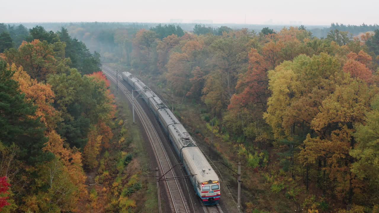 空中跟踪拍摄火车在铁路上沿着秋天的森林行驶。视频下载