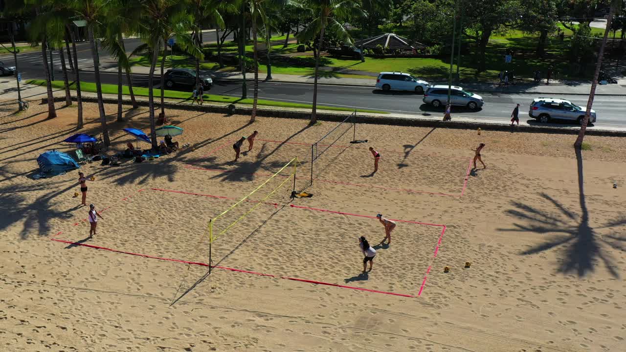 空中平移拍摄的人在沙滩上打排球，车辆在树木中的道路上移动-瓦胡岛，夏威夷视频下载