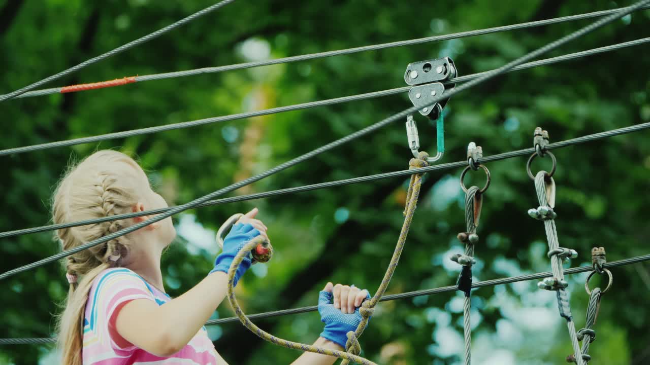夏令营的娱乐活动——孩子学习使用保险电缆，爬到高高的树枝上视频素材