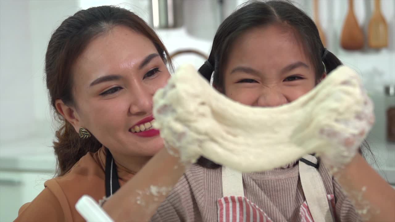 亚洲母亲和女儿正在互相帮助做面包或在厨房里烤的乐趣。反映了母亲对女儿的爱。视频下载