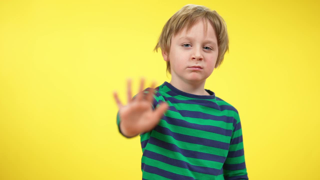金发可爱的小孩示意不看镜头。一个可爱的白人小男孩在黄色背景下摆姿势的肖像。拒绝和拒绝的概念。视频下载
