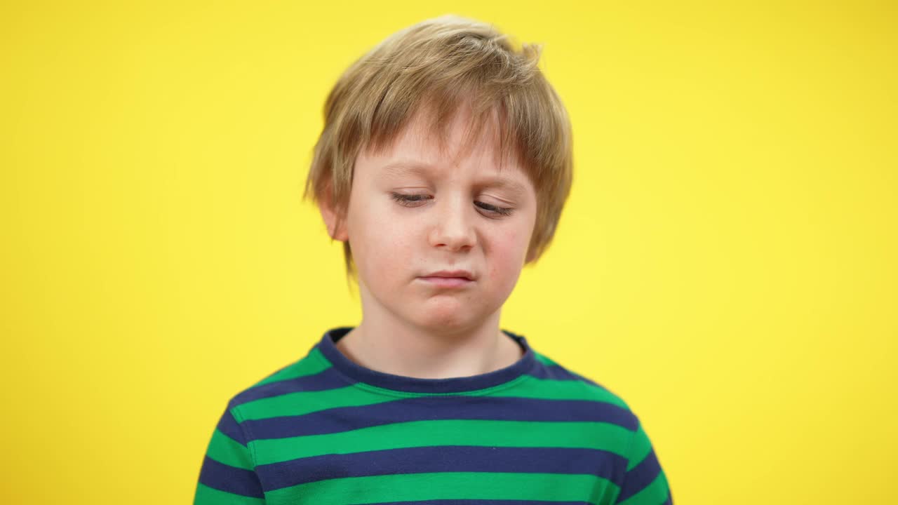 特写肖像疲惫的小男孩打哈欠在黄色的背景。精疲力竭的金发白种人孩子，脸上带着悲伤的表情。疲劳和疲惫的概念。视频下载