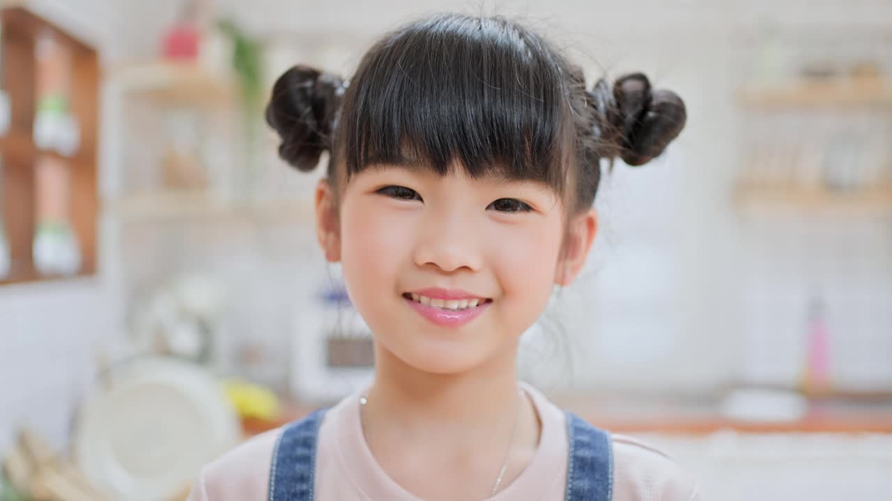 亚洲可爱的小孩拿着一杯牛奶在家里的厨房里喝。幼小的学前班女孩或女儿弄乱了乳白色的胡子和嘴唇，然后看着家里的摄像机。视频下载