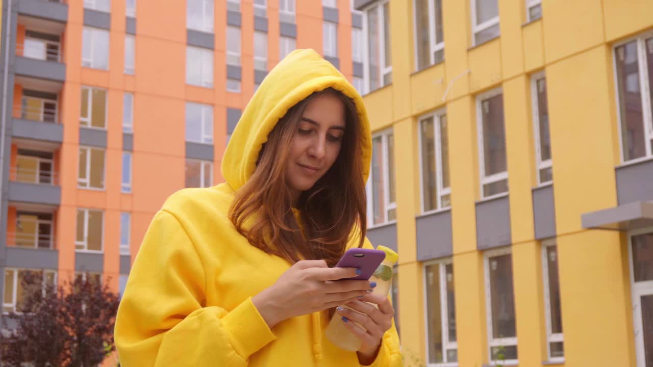 都市女性心情好，手里拿着智能手机和一瓶果汁在城市里散步视频下载