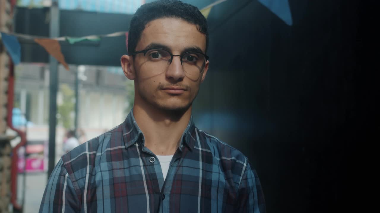 慢动作肖像迷人的中东男子戴着眼镜看着镜头，带着淡淡的微笑视频下载