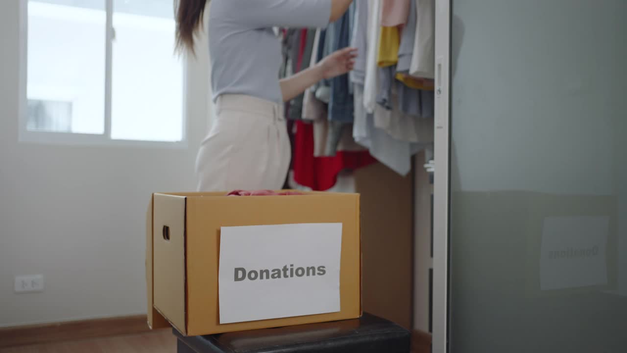 一名亚洲妇女正站在更衣室的衣柜附近，拿着一箱捐赠的衣服要送到捐赠中心。视频素材