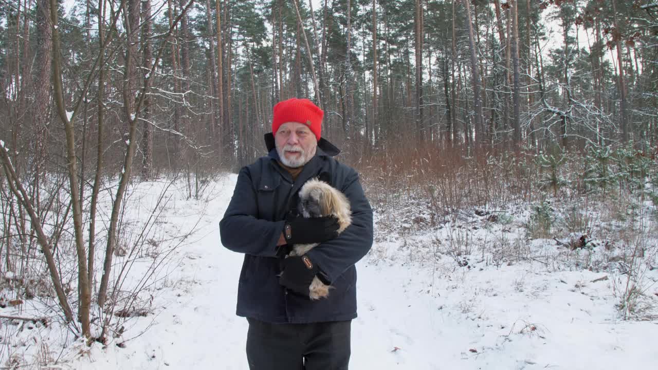 一位蓄着胡须的老人牵着狗走在雪地上视频下载
