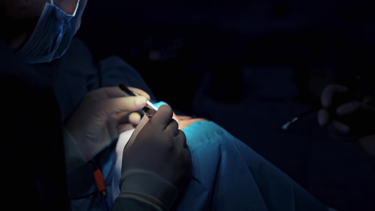 眼睑整容术的医生。外科医生正在给眼睛做手术。对抗衰老的眼睑面部矫正。在昏暗背景下的医疗灯下进行手术。特写镜头。视频下载