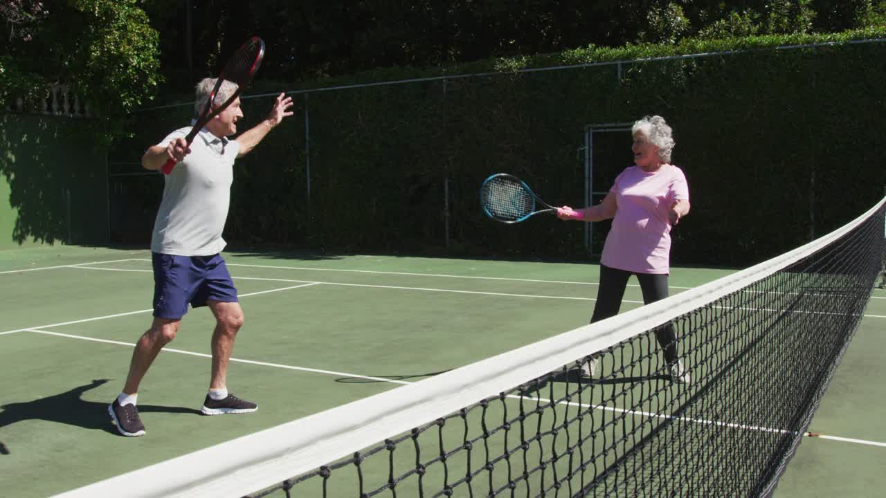 快乐的白人老年夫妇拥抱在户外网球场在玩游戏后的太阳视频下载
