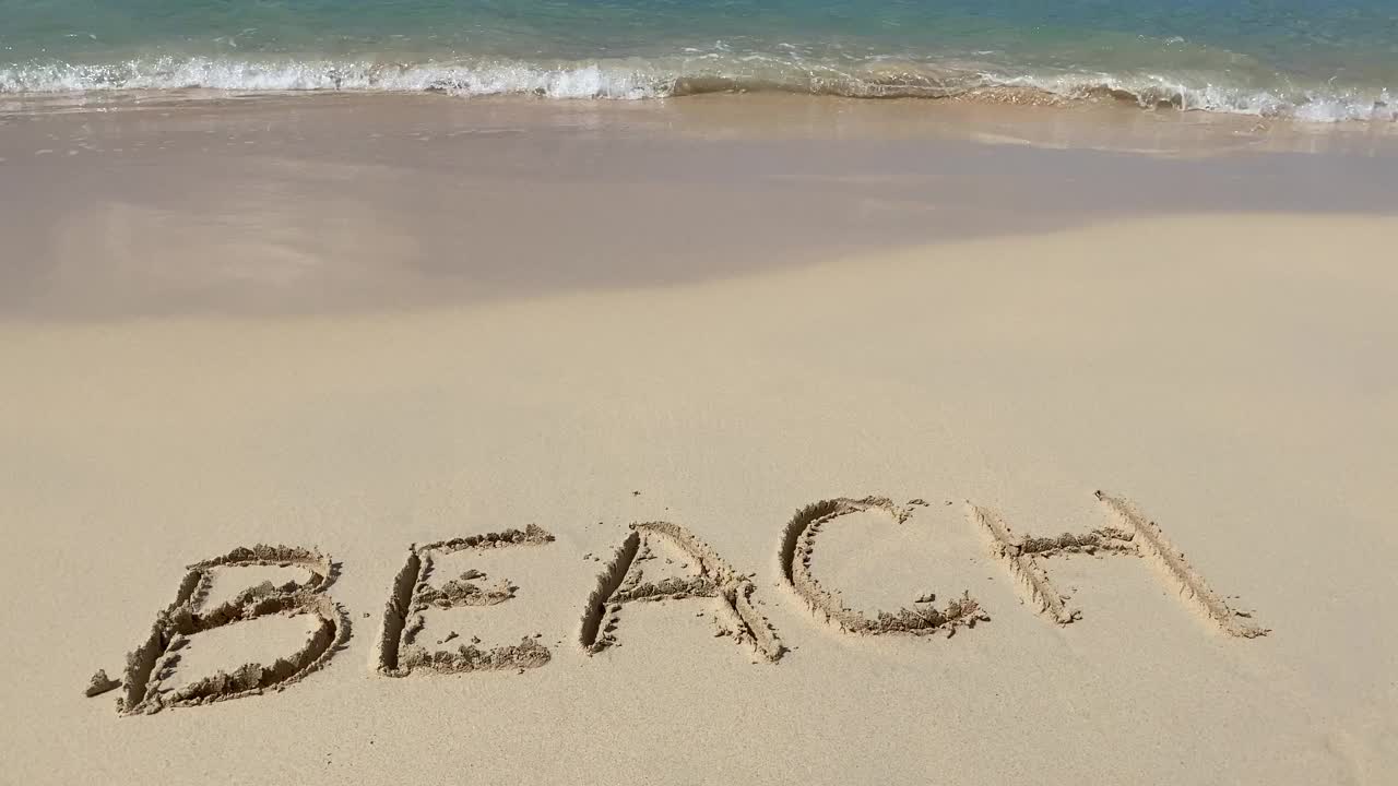 海浪在沙滩上刻下的沙滩铭文是慢动作的。假期和假期的概念视频下载