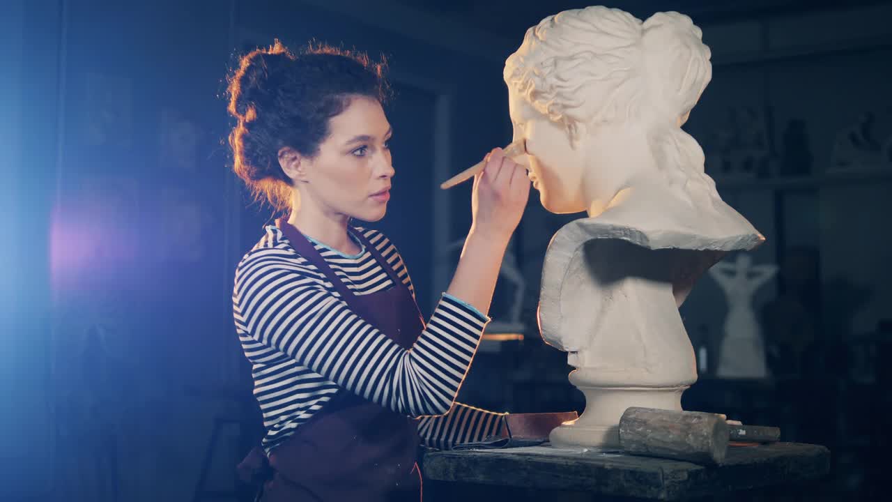 女艺术家正在用画笔照料一个石膏雕塑。艺术概念，设计工作室艺术家作品。视频下载