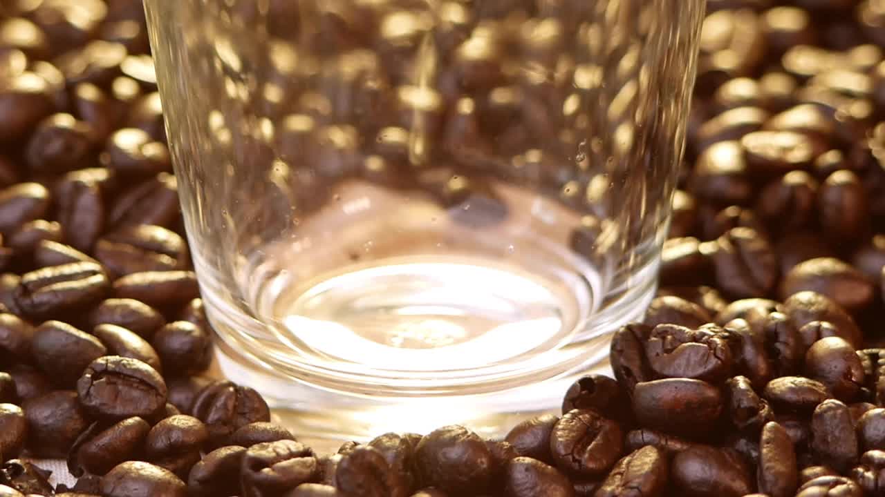 向玻璃杯中倒入热水，在新鲜烘培的咖啡豆上煮出速溶咖啡。新鲜的早晨热咖啡即将结束。视频下载