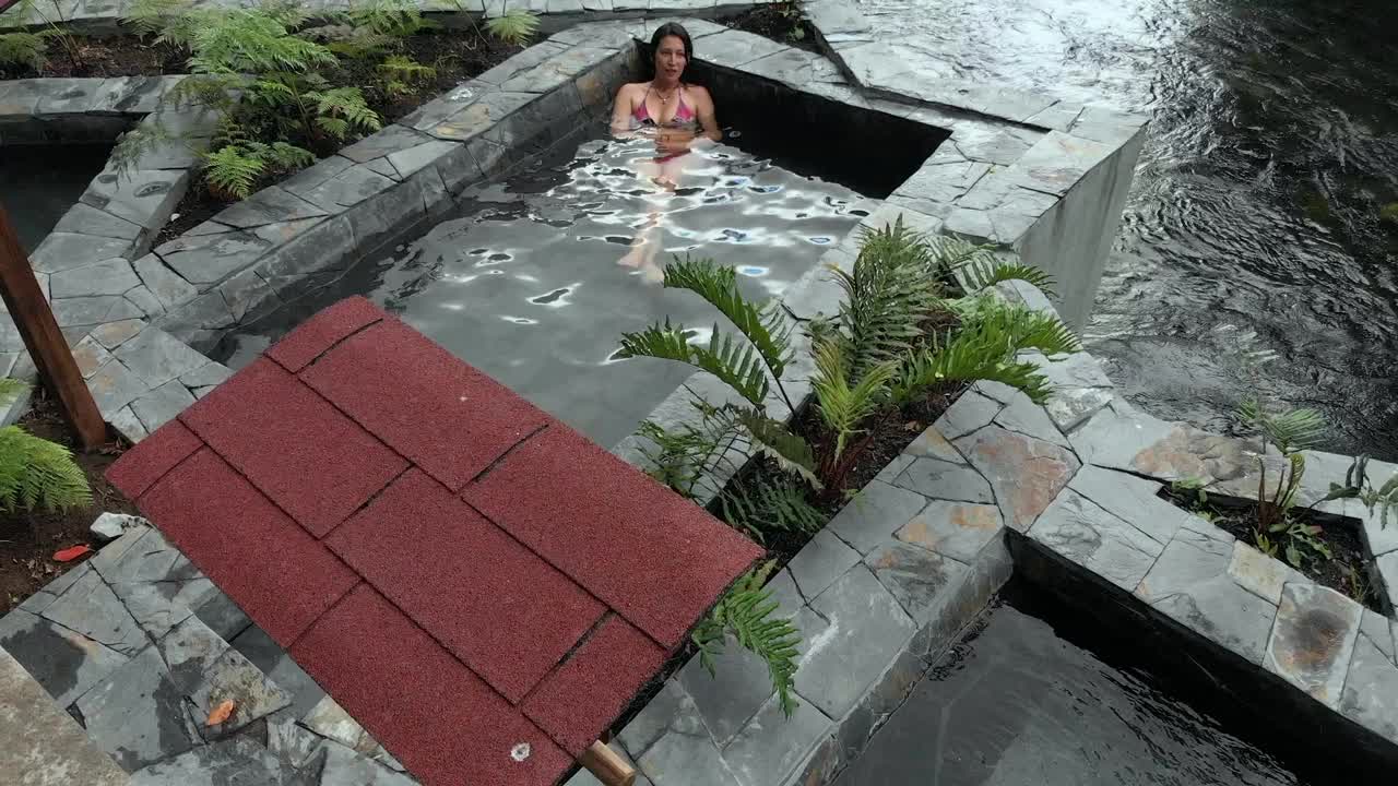 一个穿着比基尼的女人在河边的一个小热水池里休息的鸟瞰图视频下载