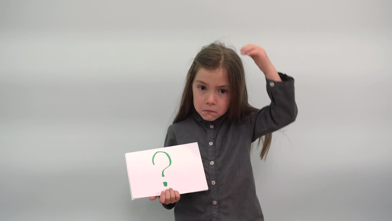 女孩有一张纸和一个问号划伤她的头的孩子想举着牌子问题灰蓝色背景孩子快乐幸福的家庭视频下载
