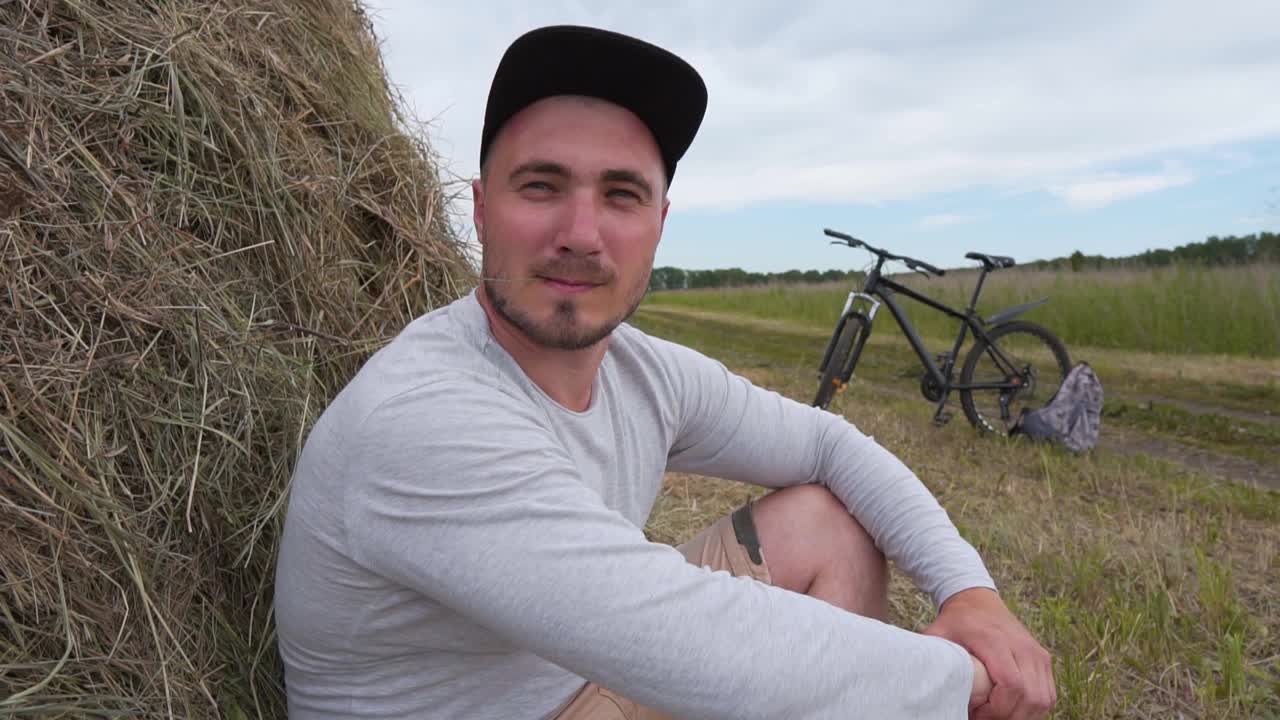 一个骑自行车的人休息在一个干草堆附近的肖像，自行车站在背景。自行车概念，活动休闲概念。自由旅行者骑自行车旅行。骑单车的健康人士视频下载