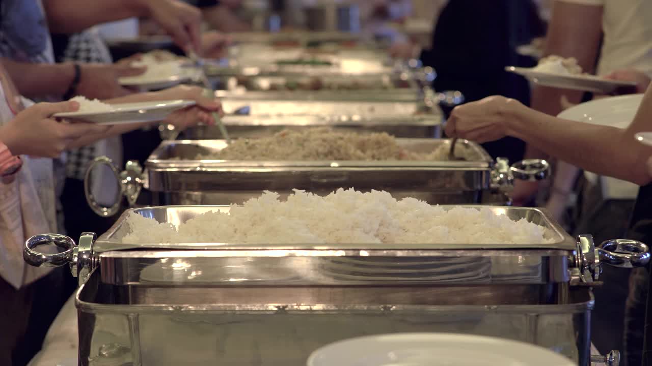 一群人在自助餐队伍中排队舀食物。专注于每个舀食物的人的手。视频下载