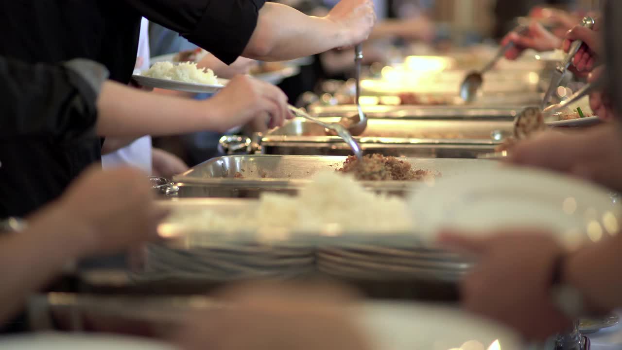 一群人在自助餐队伍中排队舀食物。专注于每个舀食物的人的手。视频下载