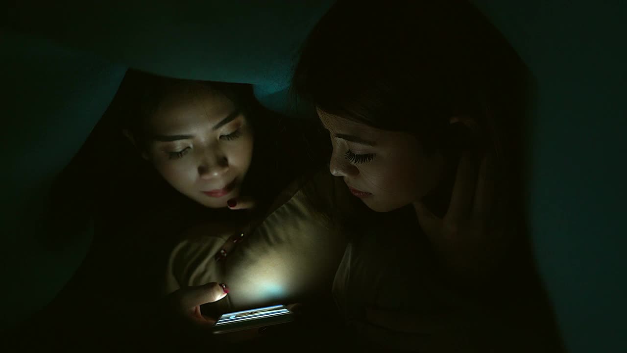 一个年轻的女孩或青少年在晚上用手机和某人说话。通过她房间里的屏幕展示了现代科技在日常生活中的运用。视频下载
