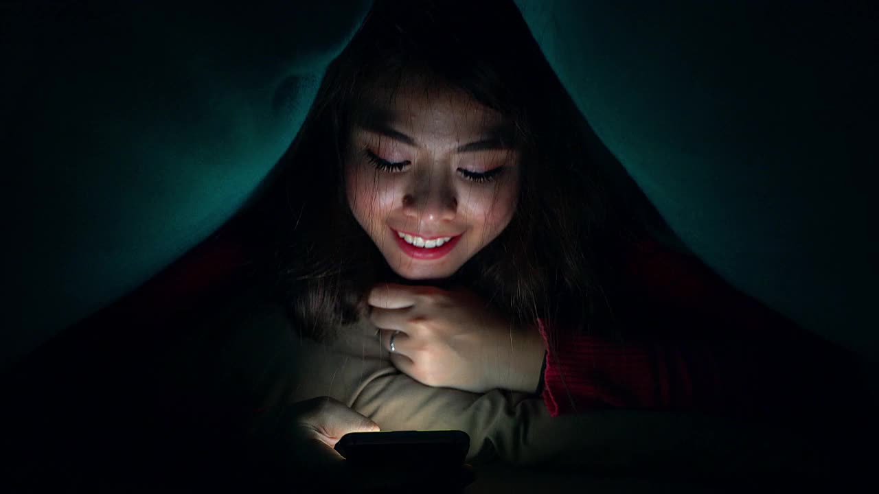 一个年轻的女孩或青少年在晚上用手机和某人说话。通过她房间里的屏幕展示了现代科技在日常生活中的运用。视频下载
