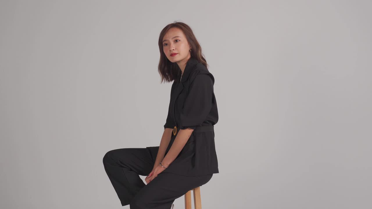 亚洲华人美丽的女人坐在椅子上微笑与灰色的背景工作室拍摄视频素材