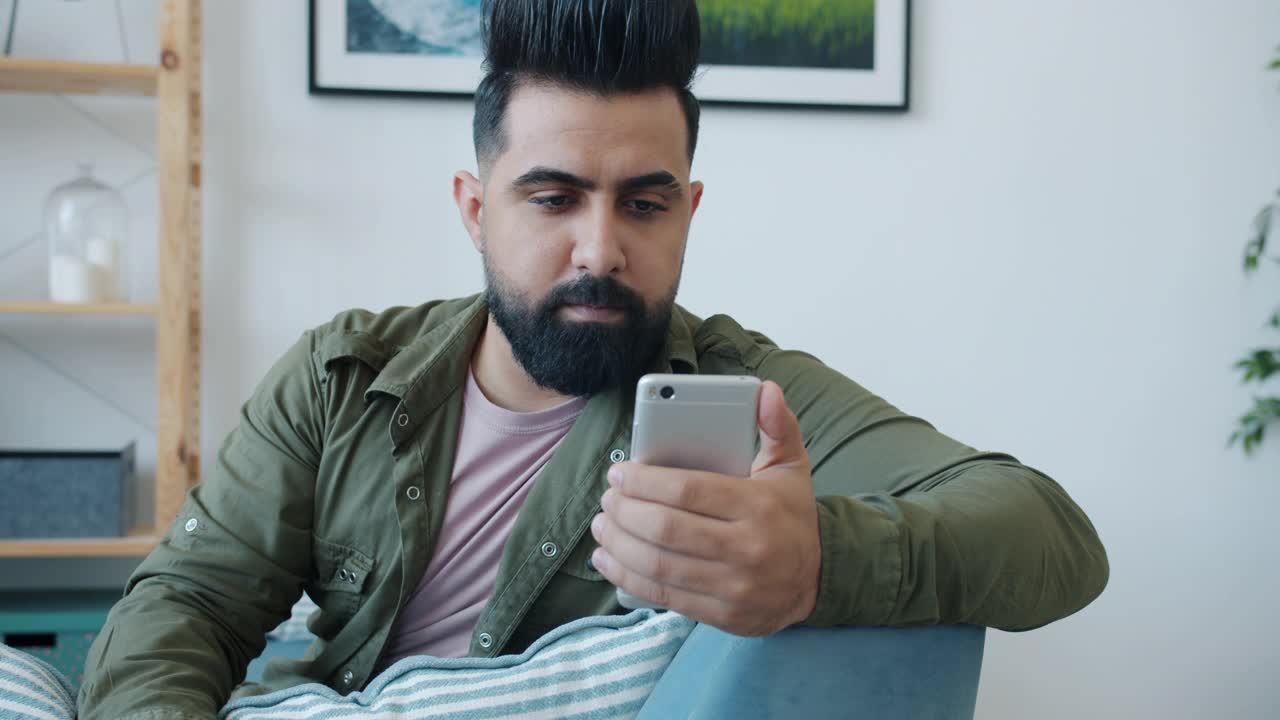 一个快乐的中东人在家里用智能手机打在线视频电话，挥手聊天视频下载