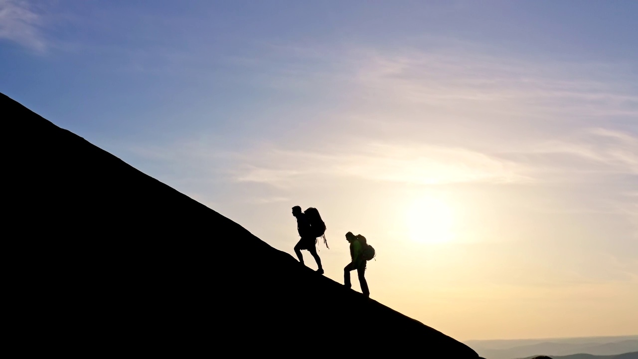 一个男人和一个女人背着背包爬上山顶的剪影。视频下载