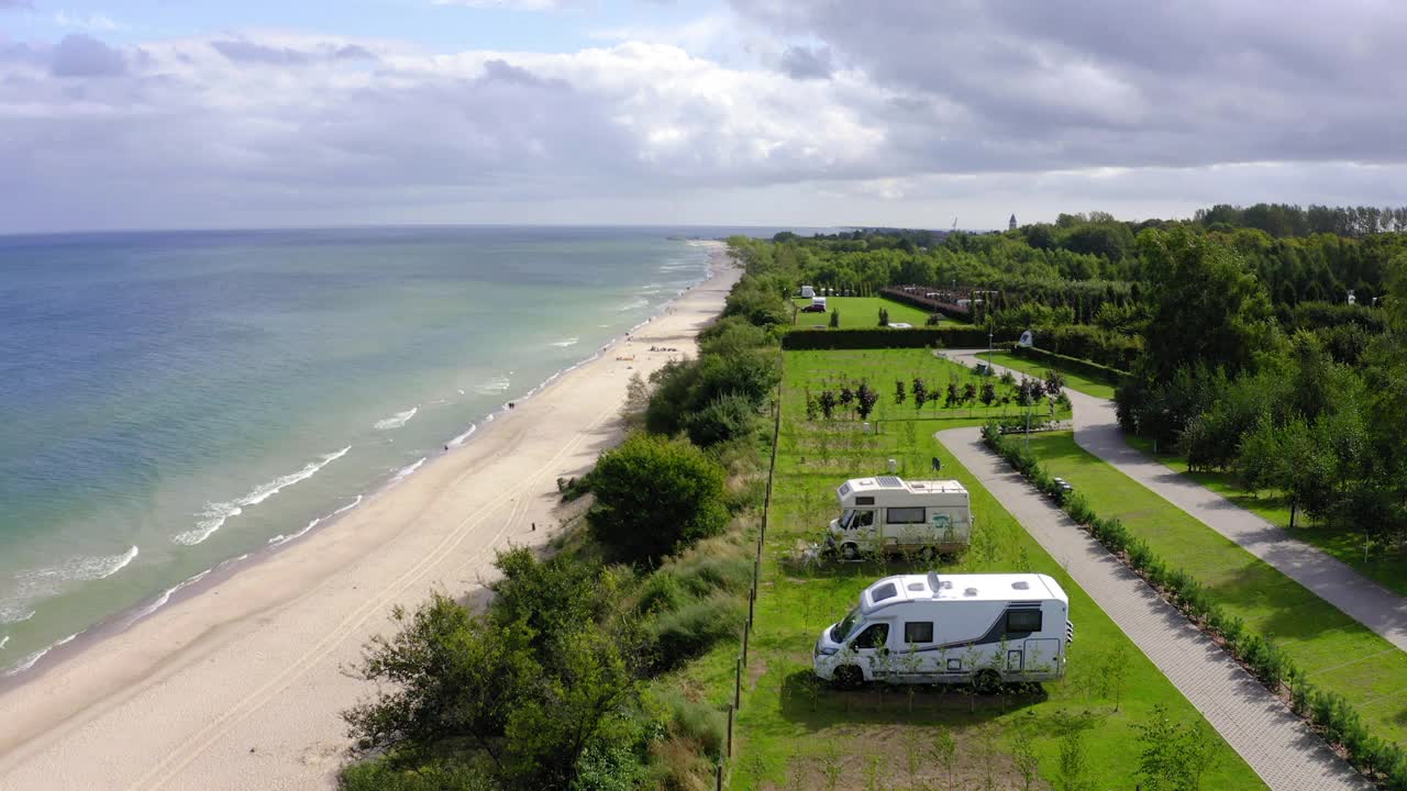 空中平移拍摄的汽车住家停在绿色景观的海滩，无人机飞过波罗的海在晴天对多云的天空视频下载