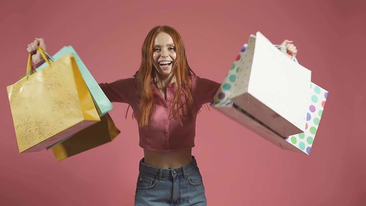 一个快乐的微笑红头发的女人拿着彩色的纸袋在一个孤立的黄色背景视频下载