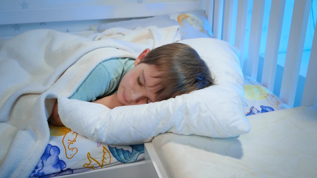 翻拍小男孩晚上穿着睡衣睡在床上，盖着白毯子的视频。孩子休息，晚上做好梦视频下载