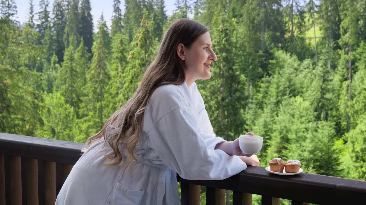 美丽微笑的女人放松在酒店穿着浴袍和在夏天的阳台上吃早餐。人们的旅游理念，夏季在山区旅游度假视频下载