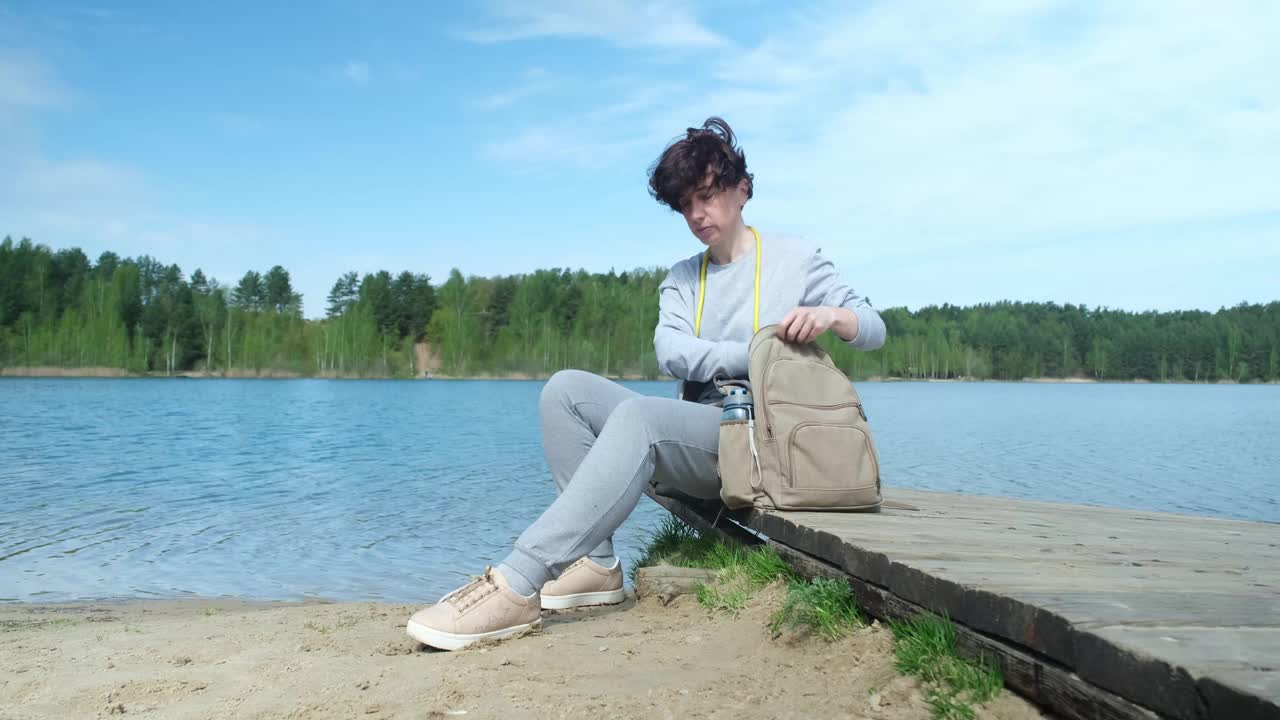 成熟的女人在湖边坐着，系着她的鞋带视频下载