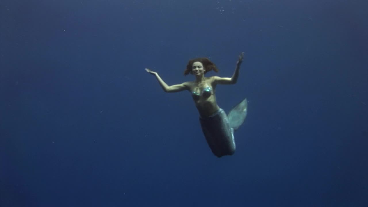 年轻女孩模型水下美人鱼服装在蓝色背景在红海摆姿势。视频下载