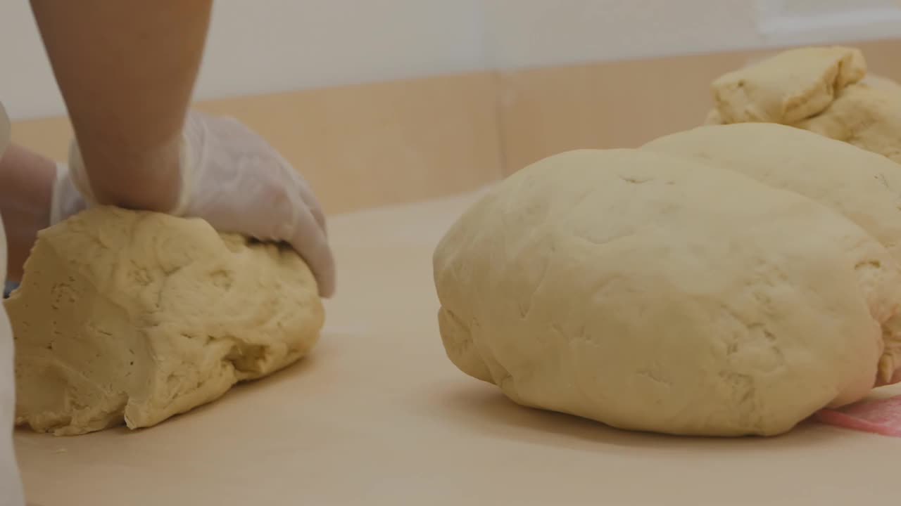 一个面包师的手揉一个有弹性的面团在桌子上烤面包的特写。面包店视频下载