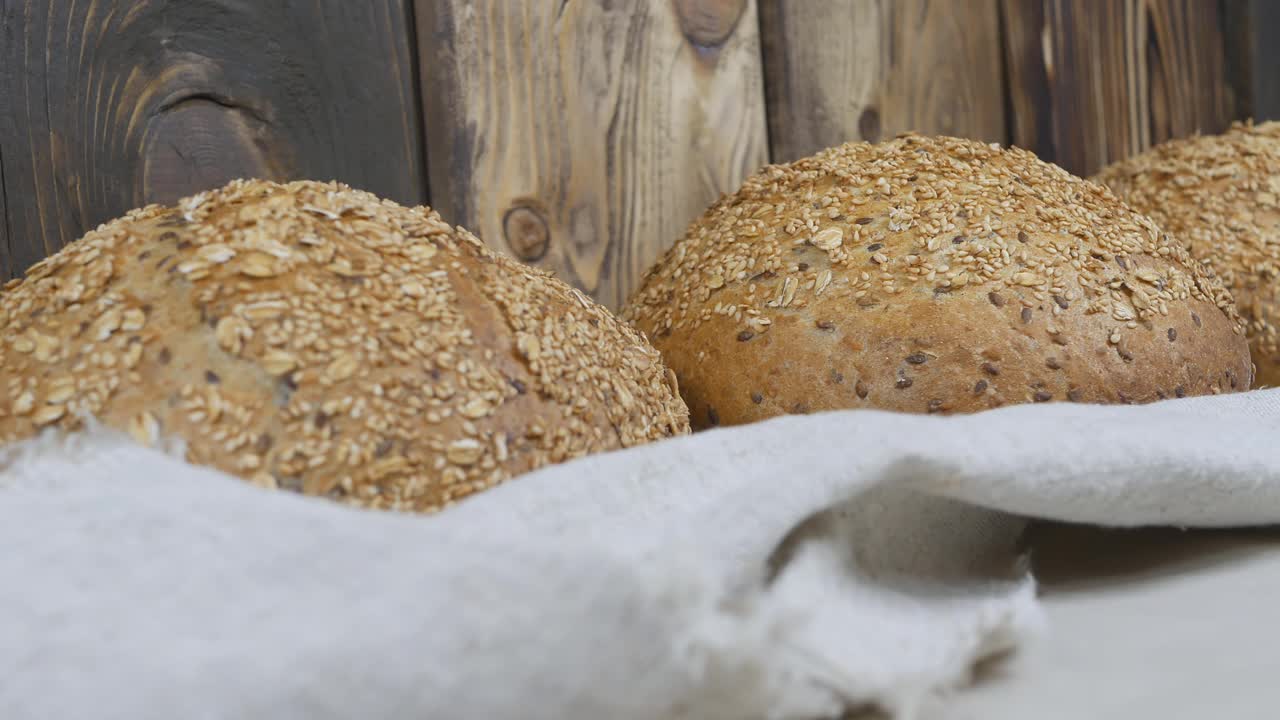 面包，许多圆面包排成一行躺在麻袋上。新鲜的面包上撒上向日葵、燕麦、亚麻和芝麻。多莉射击。特写镜头视频下载
