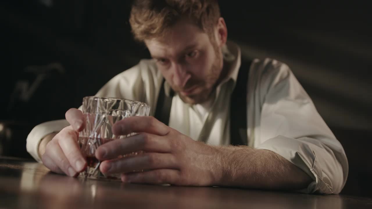 一个爱喝酒的商人坐在黑暗的酒吧里，手里拿着一杯威士忌，思考着把他带到这里的种种问题视频下载