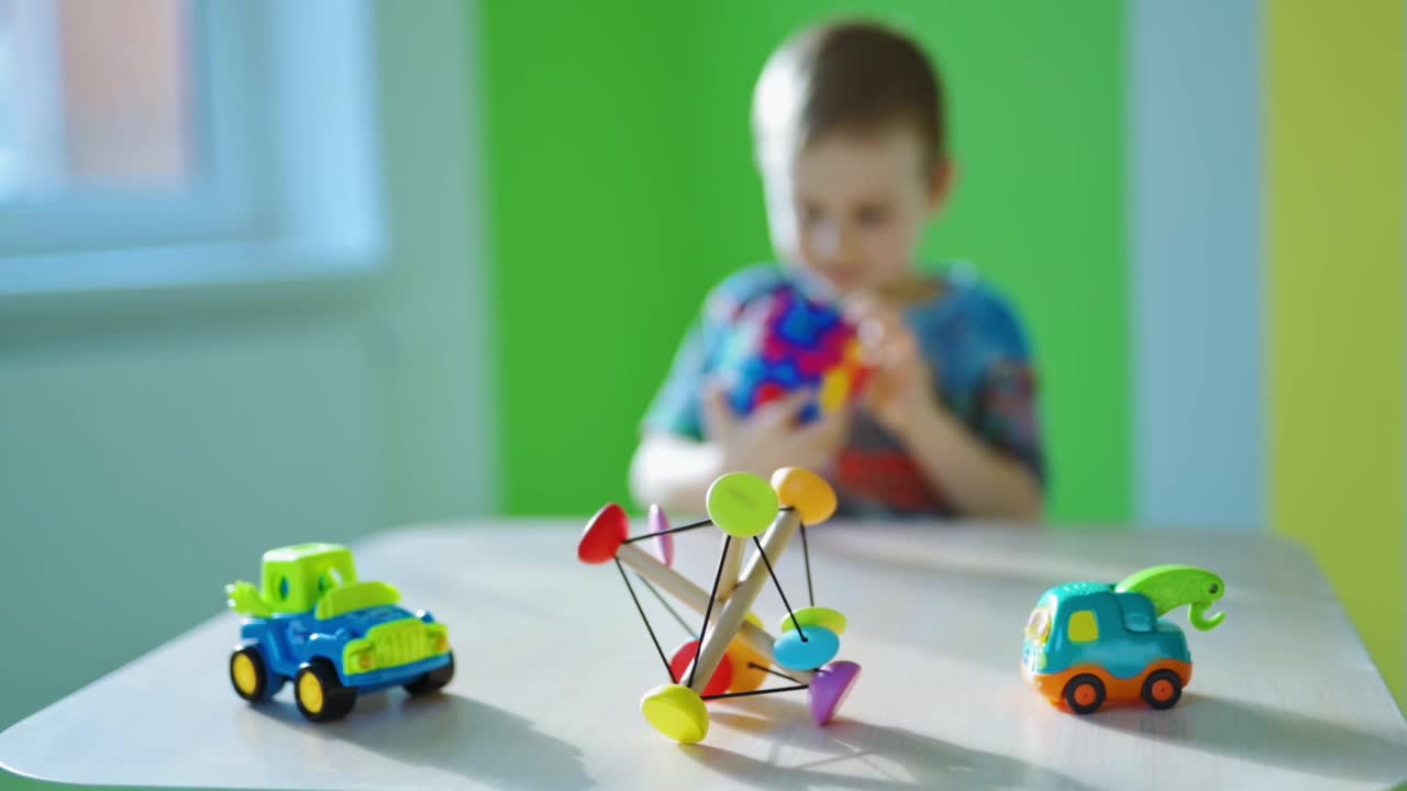 教育游戏。小男孩独自玩玩具。明亮的玩具汽车和木制玩具在木桌子上模糊的男孩背景。视频下载