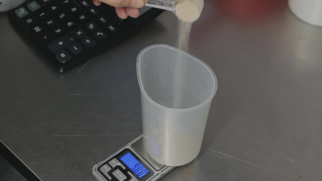 厨师用手把粉末倒进一个电子精密秤上的塑料杯里。称量烹饪配料视频下载
