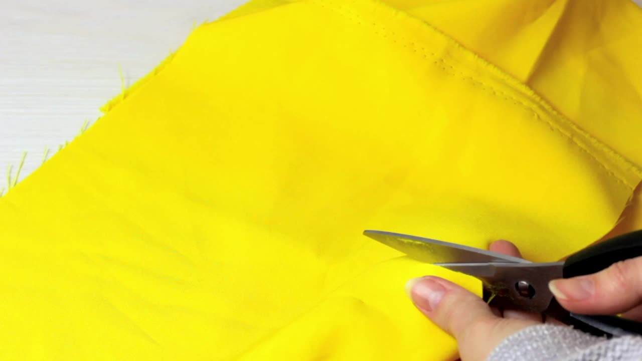 白种人妇女手切割明亮的黄色纺织品与剪刀在浅色木桌背景视频素材