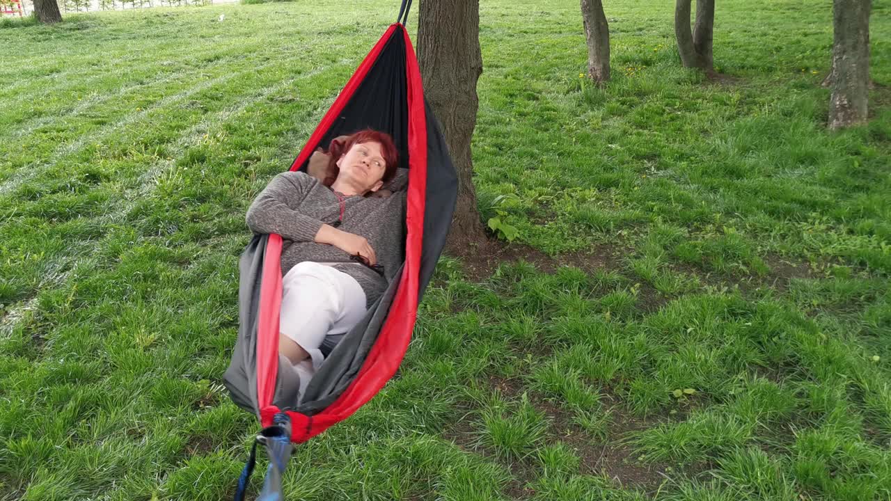 早春时节，一个女人在公园里的吊床上休息视频下载
