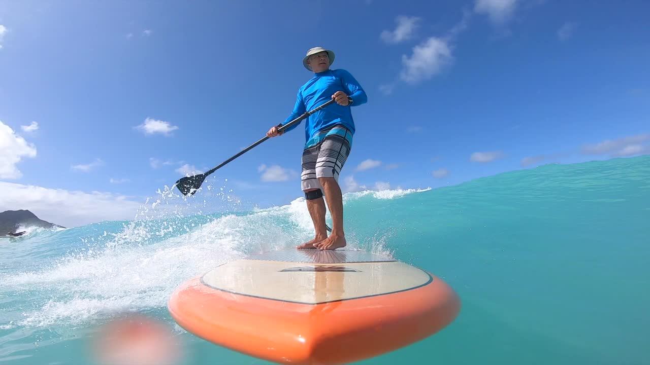 在威基基，火奴鲁鲁，瓦胡岛，夏威夷的一个橙色冲浪板上冲浪在一个SUP站着冲浪板的波。视频下载