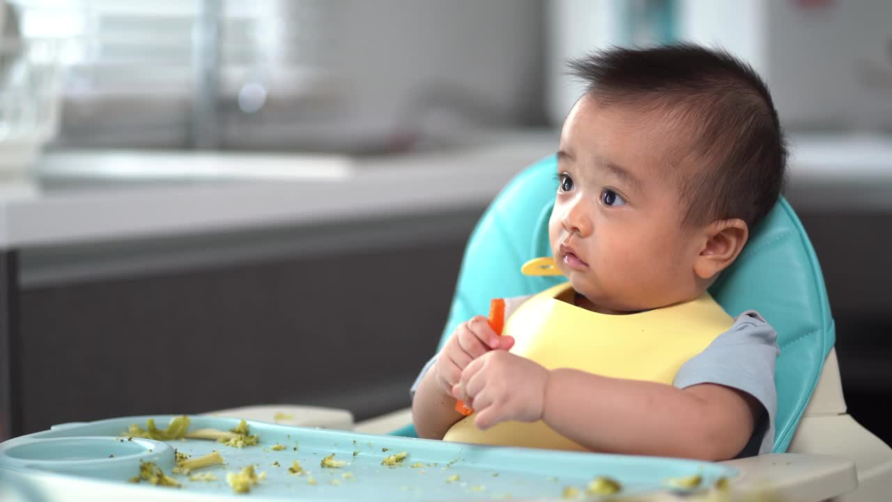 宝宝看了看手里的胡萝卜。第一次吃泥。他的亚洲小男孩的母亲喂养婴儿食品。视频下载