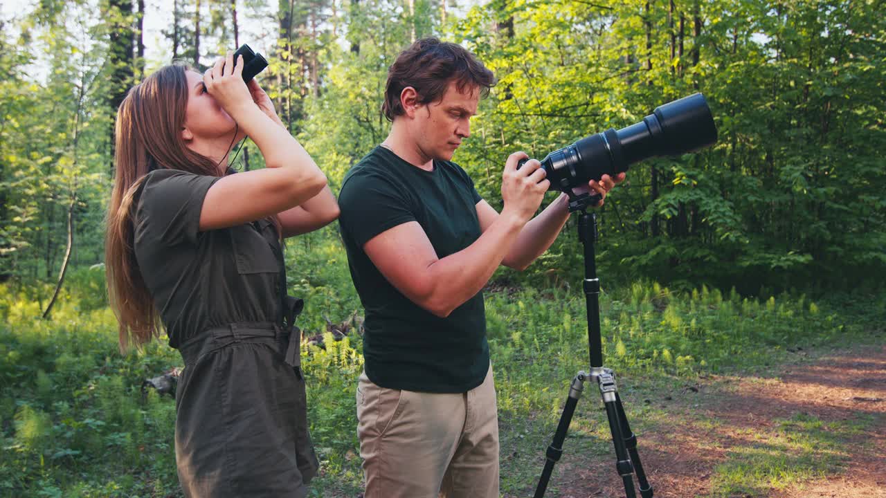 观鸟者。一对年轻夫妇在公园里看鸟。在夏季的公园里，人们用双筒望远镜和带长焦镜头的照相机来寻找鸟类视频下载