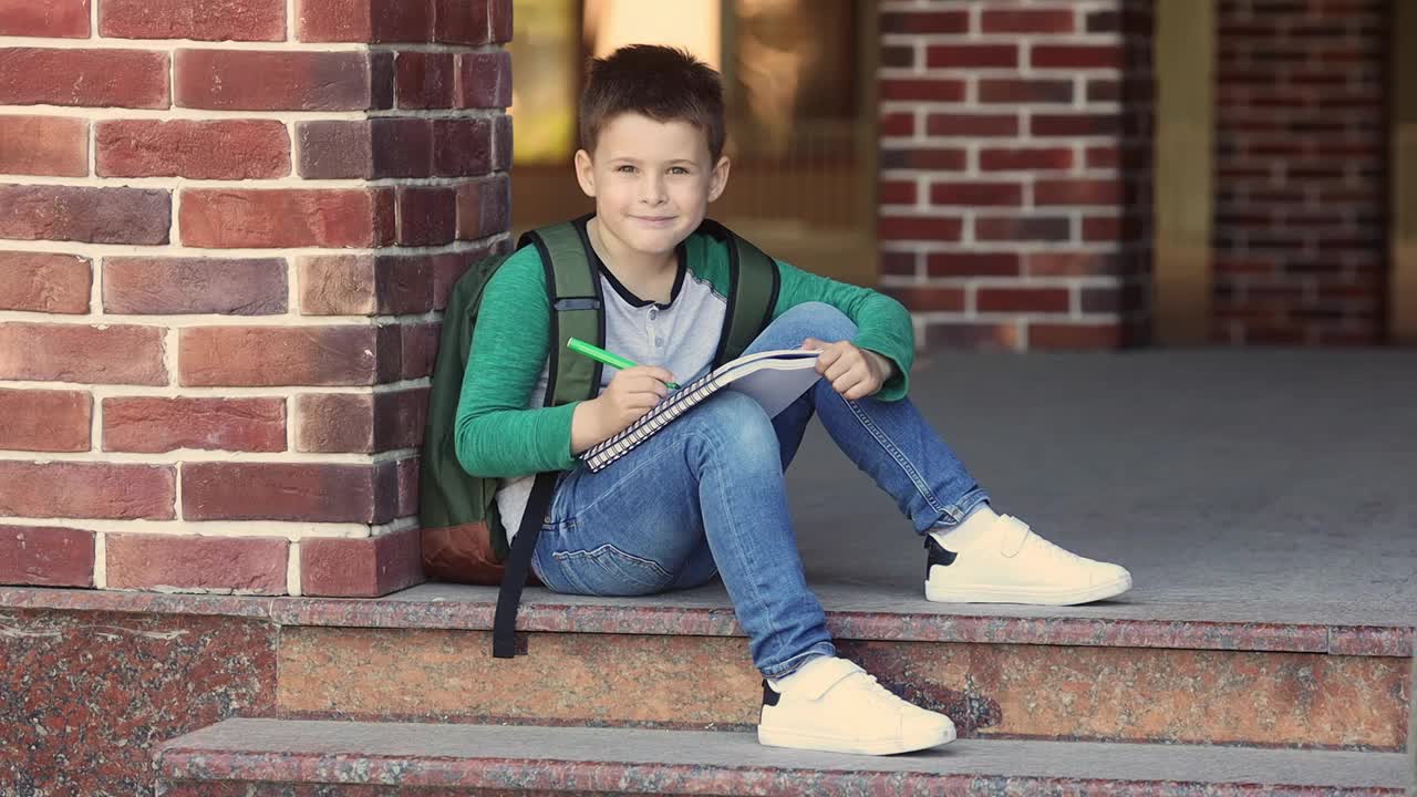 男生在校园里靠砖墙坐着做作业，等待家长视频下载