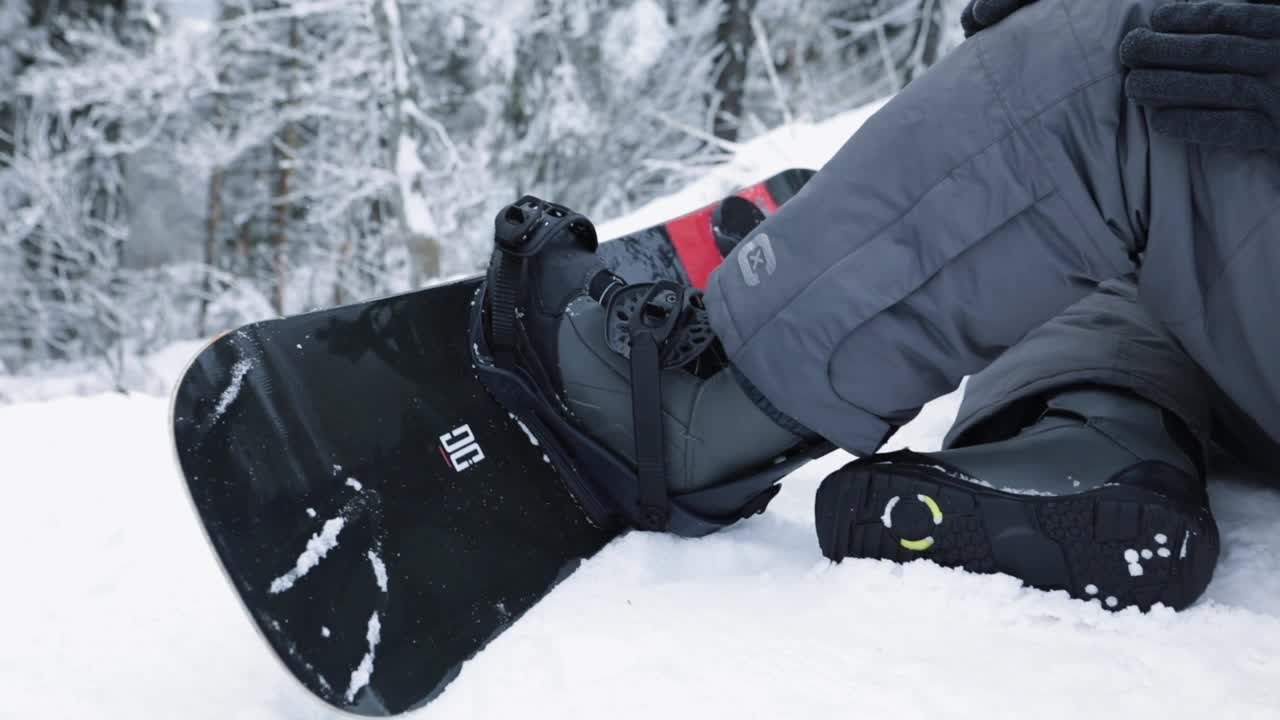 乌克兰，2020年1月20日:一名男子坐在雪山上，将靴子系在滑雪板上视频下载