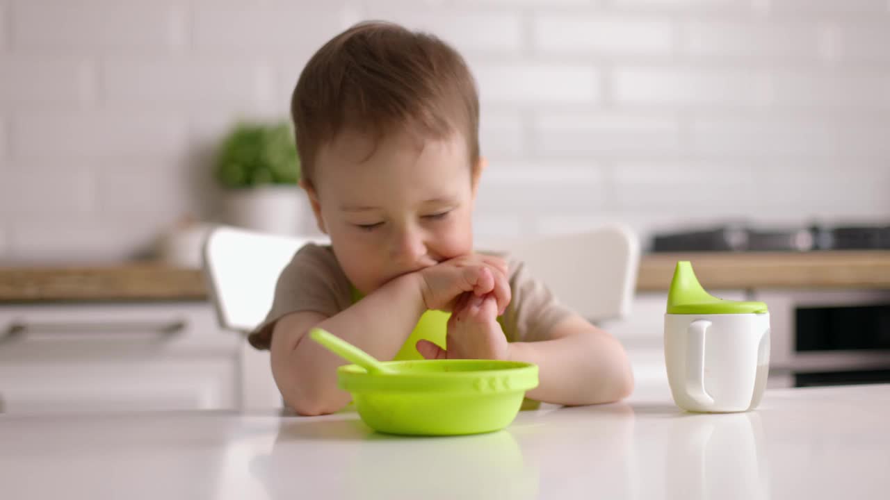 可爱的小男孩不想吃东西，摇了摇头。小孩坐在家里厨房的椅子上。视频下载
