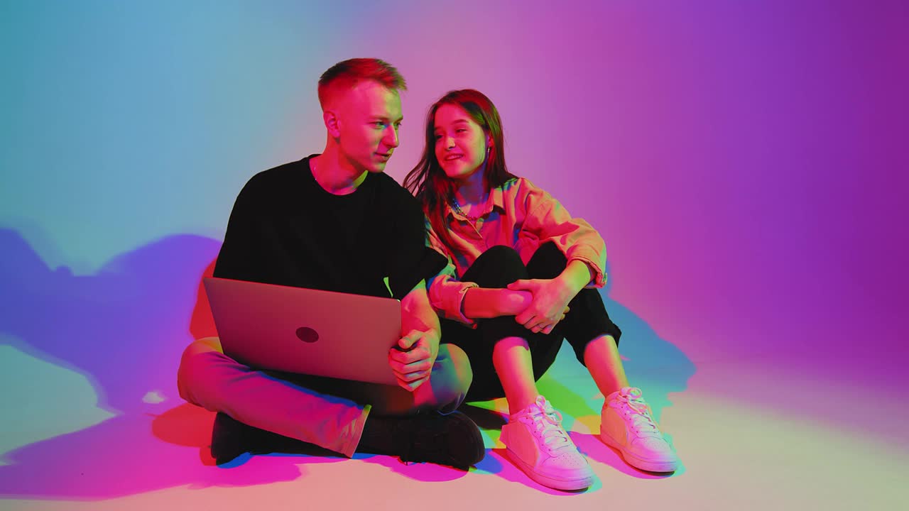 现代年轻夫妇与笔记本电脑，玩电脑，网上冲浪社交网络，网上购物。彩色的霓虹灯视频下载