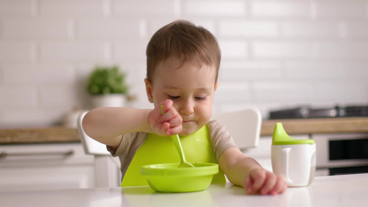 可爱的小男孩坐在桌子旁用左手吃燕麦片。左撇子孩子在家吃得很乐意。快乐的童年概念视频下载